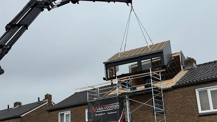 Een hijskraan die een prefab dakkapel op het dak takelt